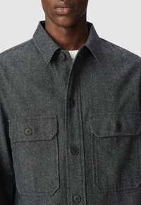Szary, teksturowany żakiet koszulowy wykonany z mieszanki wełny. Posiada kołnierz typu point, zapięcie na guziki z przodu oraz dwie kieszenie na piersi z klapkami.
