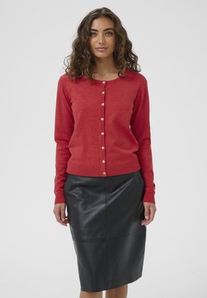 Cardigan rosso a maglia con maniche lunghe e scollo rotondo, dotato di chiusure a bottone. Abbinato a una gonna a tubino in pelle nera.