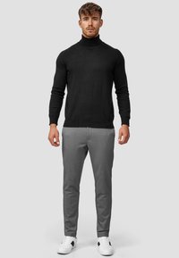 Jersey de cuello alto negro, con forma ajustada y mangas largas; combinado con pantalones de corte ajustado en gris claro y zapatillas blancas con detalles en negro.