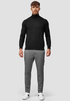 Maglione nero a collo alto, dalla forma aderente, con maniche lunghe; abbinato a pantaloni grigi chiari, sartoriali e sneakers bianche con accenti neri.
