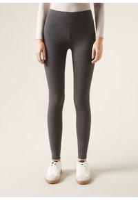 Graue Leggings mit hohem Bund, aus einem glatten, dehnbaren Stoff. Kombiniert mit weißen Sneakers mit einer beigen Sohle.
