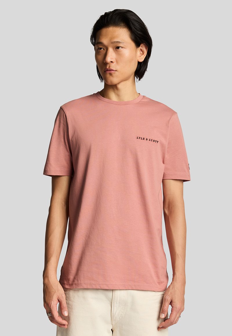 Camiseta de algodón de color rosa claro con mangas cortas, cuello redondo y texto negro "LYLE & SCOTT" en el pecho. Textura suave, diseño casual.