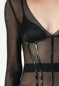 Svart mesh-top med lange ermer, dyp V-hals og glansfulle accenter. Inkluderer en tettsittende fasong med et kontrasterende strukturert underlag.