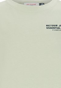 Jasnozielona bawełniana koszulka z okrągłym dekoltem i krótkimi rękawami, z granatowym nadrukiem na przodzie, z napisem "RETOUR JEANS ESSENTIAL."