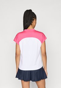 Trumpas rankovėmis polo marškinėliai, turintys rožinę viršutinę dalį ir baltą apatinę dalį, pagaminti iš lygaus audinio, derinami su plisuota tamsiai mėlyna sijonu.