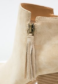 Beige suède enkelboot met een zijrits en kwastje. Voorzien van een gestructureerde houten hak en een soepele binnenvoering.