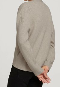 Suéter de punto beige con ajuste holgado, textura acanalada, escote profundo y hombros caídos. Cuenta con un dobladillo recto y mangas largas.