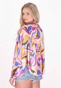 Farverig bluse med mønster i let stof, med lange ærmer og en rynket nederkant. Har lilla, lyserøde, orange og grønne svulm.