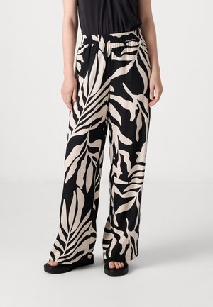 Pantalons larges noir et beige avec un motif de feuillage, présentant une taille élastique et un tissu fluide, associés à des sandales à plateforme noires.