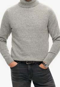 Grijze coltrui met een textuurrijk breisel, gecombineerd met een donkere spijkerbroek en een zilveren horloge met een zwarte leren band.