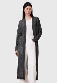Lång, öppen cardigan framtill i mörkgrått, med ett texturerat m�önster, långa ärmar och sidoflikar, bärs över en ljus topp och krämfärgade byxor.
