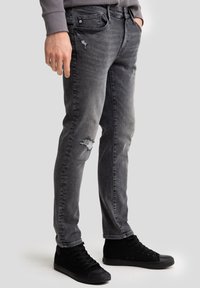 Vaqueros de mezclilla gris con un ajuste slim, detalles desgastados y un sutil desvanecimiento. Combinados con zapatillas negras de caña alta.