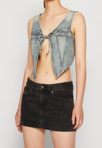 Denim crop top med V-udskæring, frontbåndslukning og to brystlommer. Bæret sammen med en sort denim mini skirt.