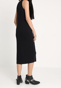 Czarna midi sukienka o bezrękawowym kroju, gładkiej fakturze i prostym cięciu. W połączeniu z czarnymi botkami za kostkę, które mają srebrne akcenty i paski.