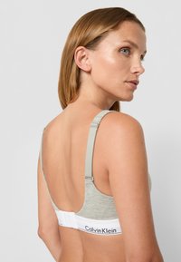 Pilkas audinio liemenėlė su reguliuojamomis petnešėlėmis, glotnaus paviršiaus ir balta juosta su "Calvin Klein" logotipu, sukurta patogumui ir palaikymui.