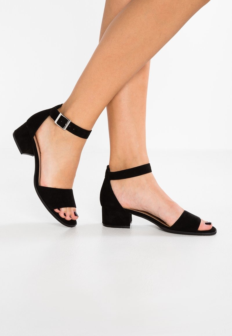 Sandales à talon carré en daim noir avec une bride de cheville. Design à bout ouvert avec une texture lisse et un petit accent de boucle.