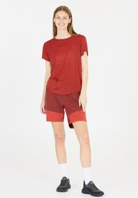 Rødstribet T-shirt med en afslappet pasform, parret med røde shorts med farveblokdesign. Model iført sorte teksturerede sneakers og hvide sokker.