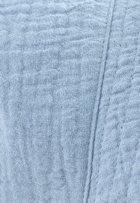 Gaiši zils teksturēts audums ar austa rakstu un izšūtu šuvi, kas vertikāli stiepjas labajā pusē.