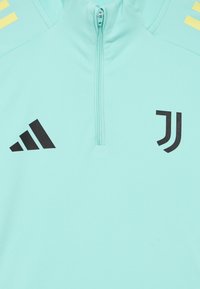 Top sport verde mentă cu fermoar de un sfert, cu logo-urile negre Adidas și Juventus. Textură netedă, design minimalist.