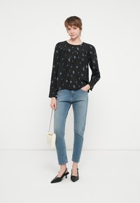 Svart langermet bluse med blå blomstertrykk, med plisserte detaljer, kombinert med lyseblå smale jeans og svarte spisse hæler.