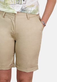 Pantalones cortos de algodón beige con dobladillo enrollado, delantero plano y bolsillos laterales, que presentan una textura suave y un ajuste a medida.