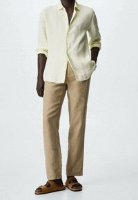 Chemise en lin jaune pâle, coupe ample ; pantalon en lin beige à coupe droite ; sandales marron à double bride et semelle plate.