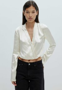 Crème-kleurige satijnen wikkeltop met lange mouwen, diepe V-halslijn en cropped lengte, gecombineerd met hoge taille zwarte denim jeans.