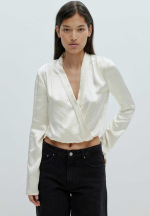 Crème-kleurige satijnen wikkeltop met lange mouwen, diepe V-halslijn en cropped lengte, gecombineerd met hoge taille zwarte denim jeans.