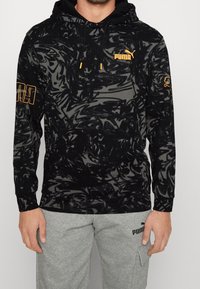 Czarna bluza z kapturem z abstrakcyjnym czarno-szarym wzorem w spirale, żółte logo Pumy na klatce piersiowej i rękawie, przednia kieszeń kangurka, kaptur ze sznurkiem.