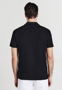 Polo shirt nero a maniche corte con una finitura testurizzata e colletto. Nessun marchio visibile, design pulito con orlo dritto e vestibilità rilassata.