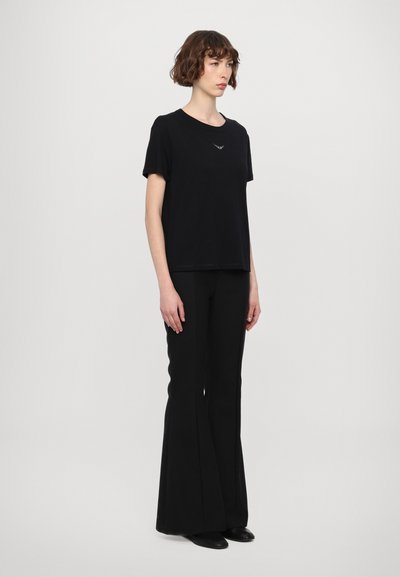T-shirt noir à manches courtes en tissu doux, avec un col rond et un petit détail graphique. Associé avec un pantalon évasé noir.