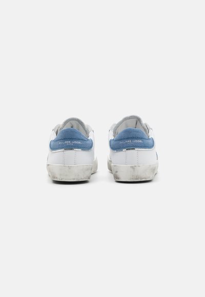 Weiße Sneakers mit blauen Wildlederakzenten und grauem Element an der Ferse. Verfügt über eine strukturierte Sohle und ein leicht abgenutztes Erscheinungsbild.