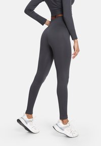 Tmavošedé legíny s vysokým pásom z elastického materiálu, s priliehavým strihom a v kombinácii s bielymi športovými topánkami.