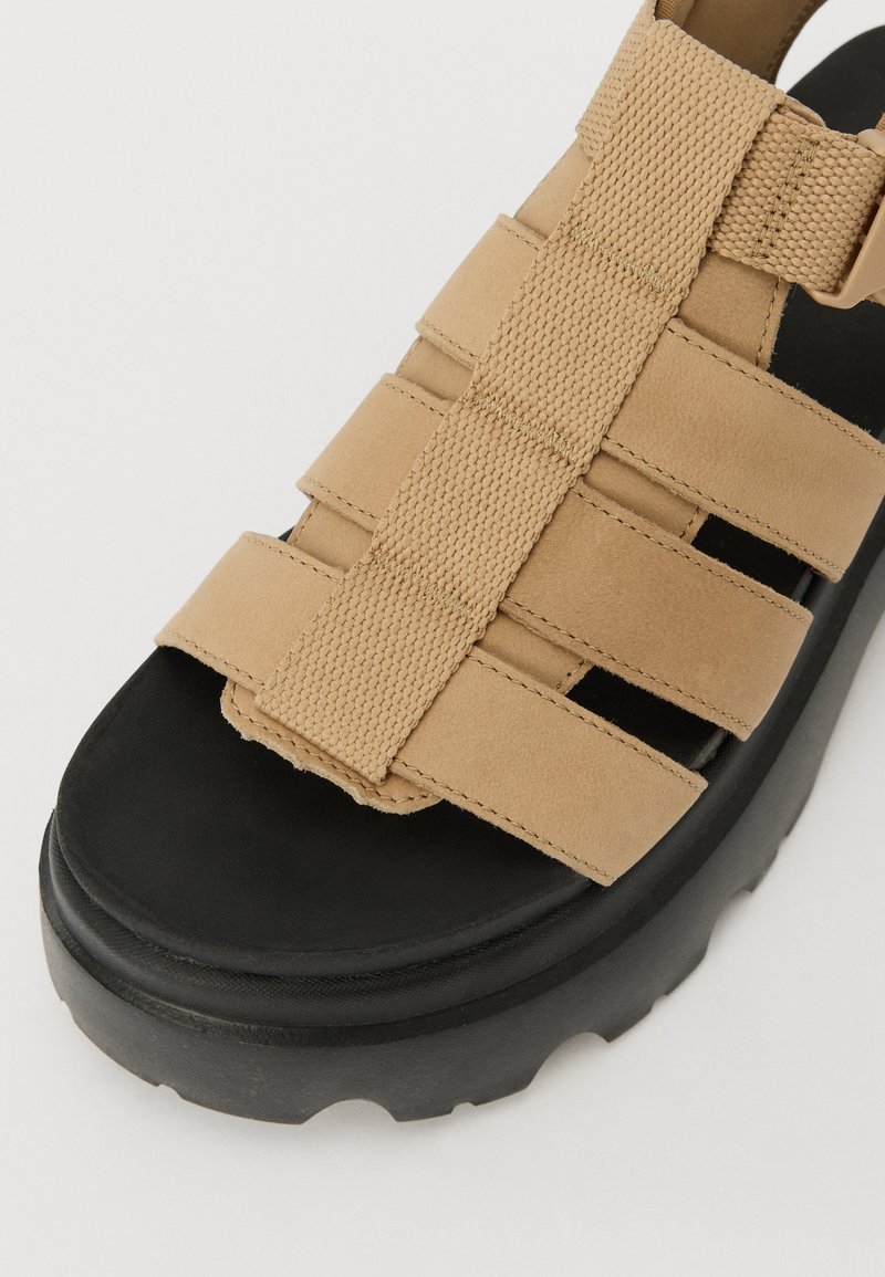 Beige Sandalen mit elastischen Riemen und gepolstertem Obermaterial. Eigenschaften einer dicken, schwarzen Plattformsohle mit strukturiertem Finish.