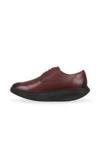 Zapato de cuero marrón con puntera redondeada, que presenta costuras mínimas y una suela de goma negra texturizada. Diseño elegante con un acabado suave.