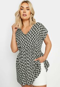 Svart och vit prickig tunika med V-ringning, korta ärmar och rynkad midja. Materialet är lätt och flödande med sidofickor.