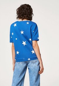 Camiseta de algodón azul de corte relajado, con patrones de estrellas blancas y escote redondeado. Combinada con jeans de denim azul claro.