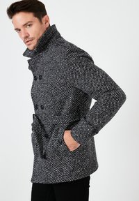 Peacoat in misto lana con un motivo houndstooth bianco e nero, caratterizzato da un collo alto, chiusura doppiopetto e tasche laterali.