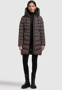 Donkergrijze pufferjas, voorzien van een capuchon, ritssluiting en elastische manchetten. Draagt over een zwarte top en gecombineerd met zwarte chunky boots.