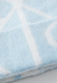 Lys blå ullstoff med en myk tekstur som har hvite geometriske mønstre. Stoffet har en litt fluffy finish som antyder varme.