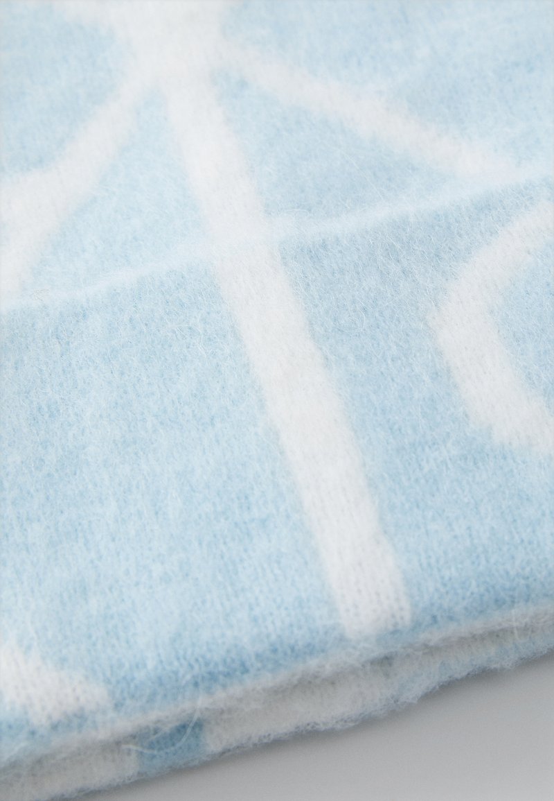Tissu en laine bleu clair avec une texture douce, présentant des motifs géométriques blancs. Le tissu a une finition légèrement duveteuse, suggérant de la chaleur.
