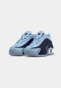 Hellblaue Sportschuhe mit marineblauen Akzenten, die ein perforiertes Obermaterial, strukturierte Details und ein sichtbares Dämpfungssystem in der Sohle aufweisen.