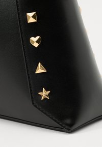 Black synthetic handbag featuring gold metal embellishments: square, heart, pyramid, and star studs; smooth texture and angular shape.