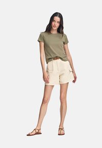 T-shirt a maniche corte verde oliva abbinato a pantaloni cargo beige, con cintura, esposto su uno sfondo neutro. Sandali piatti completano il look.
