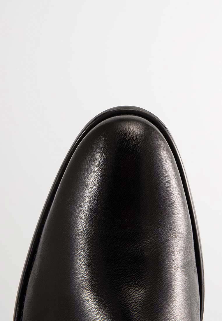 Schwarzer, polierter Leder-Schuh mit glatter Oberfläche und abgerundeter Form auf einem schlichten, hellen Hintergrund.