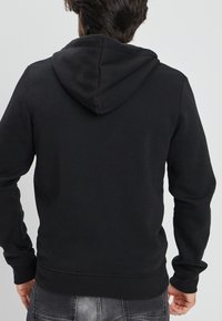 Sudadera negra con bolsillo canguro, puños y cintura de canalé. Fabricada con tela suave; cuenta con una capucha cosida en la parte posterior.