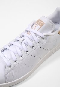 Vit läder sneaker med texturerad ovandel, rund tå, platta vita snören, perforerade detaljer på sidorna och beige accent på klacken.