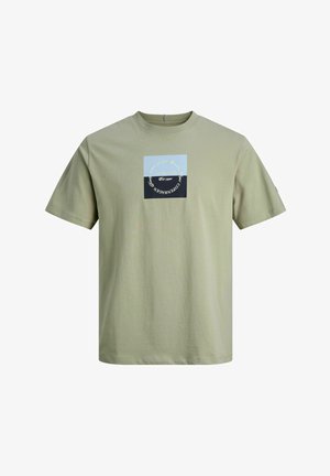 Felpa con cappuccio blu navy con zip, t-shirt verde chiaro con patch grafico, jeans blu larghi e sneakers grigie con dettagli neri.