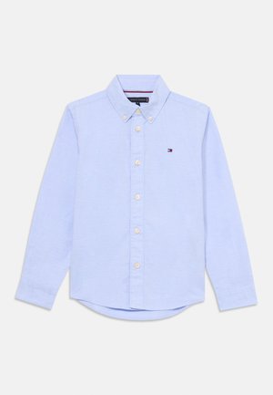Chemise à manches longues bleu clair avec col à boutonnière, cinq boutons, ourlet arrondi et petit logo brodé sur la poitrine. Tissu en coton.