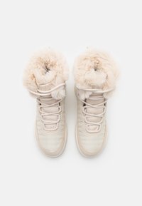 Light beige high-top boots with furry ankle collar, textile upper, flat laces, and rubber soles designed for warmth and comfort.